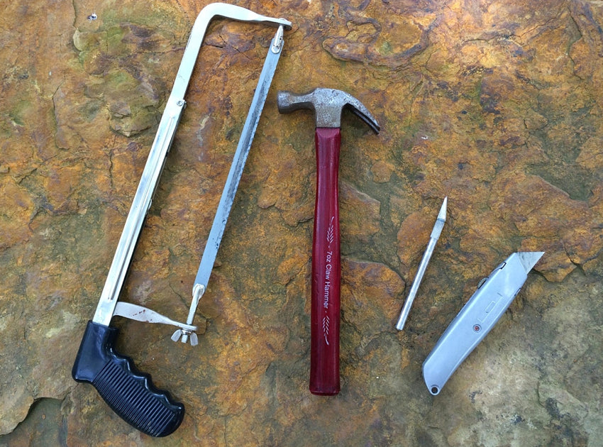 A hacksaw, hammer, scalpel, and utility knife placed on a stone step