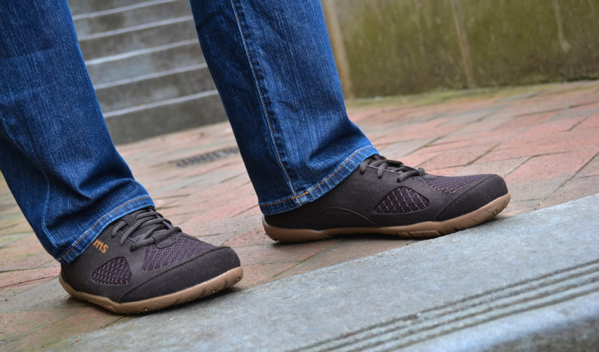 A person standing on cobblestones and wearing Lems Primal 2 Brown shoes