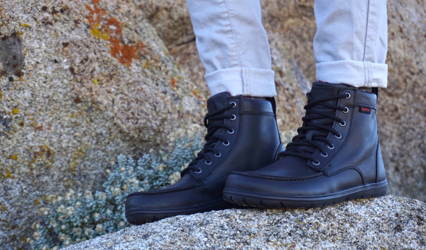 Hiker posing in a pair of Lems Boulder Boots in Leather Raven in front of colorful rocks and desert vegetation