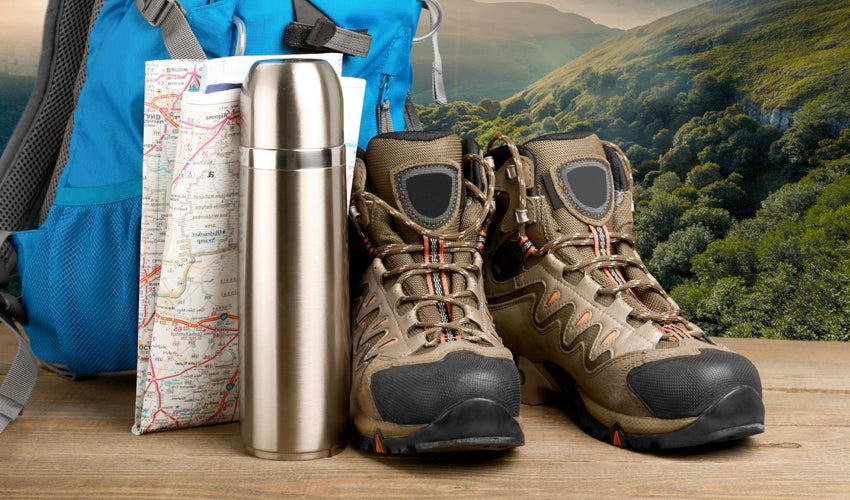 A collection of hiking gear, including conventional hiking boots, thermos, topographical map, and backpack