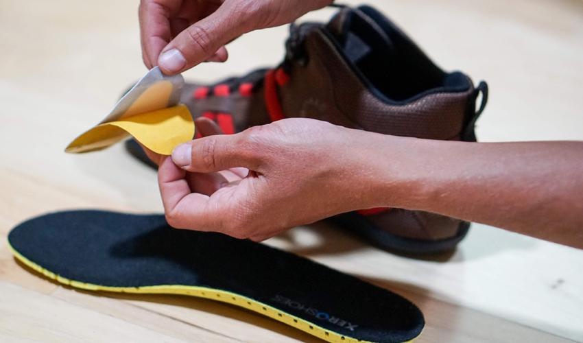 A person peeling away the adhesive covering on a pair of Pedag metatarsal pads