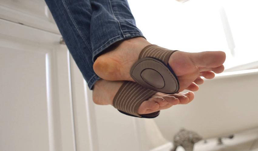A person wearing Strutz Pro Brown foot pads on bare feet sitting on a bathroom vanity with legs crossed