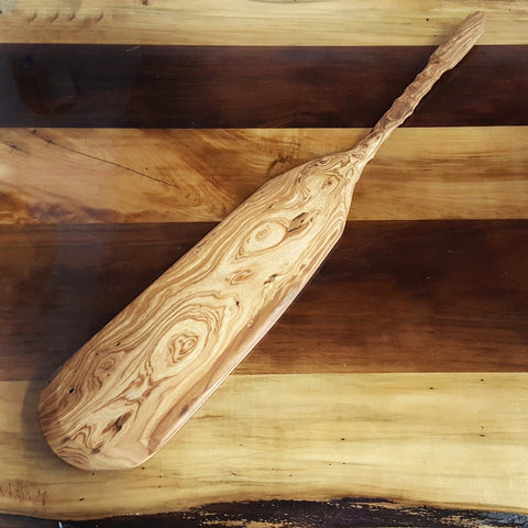 A handmade cherry charcuterie paddle against a maple and walnut tabletop