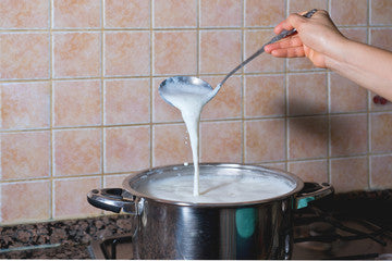 Cooking pot full of milk with metal ladle dripping milk back into the pot.