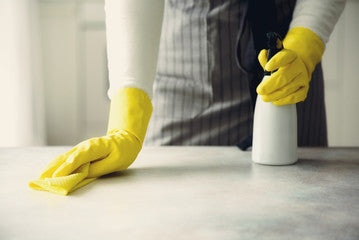 Person cleaning a surface with rubber gloves and disenfectant