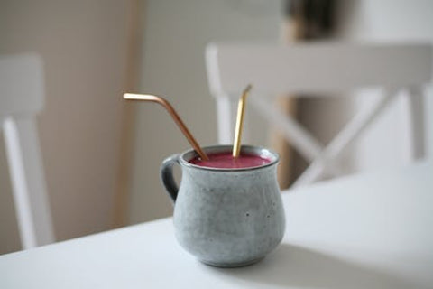 Drink in a handmade ceramic mug with two metal bent straws sticking out on a white tabletop