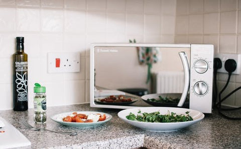 Microwave with plates of food on white plates on a speckled countertop