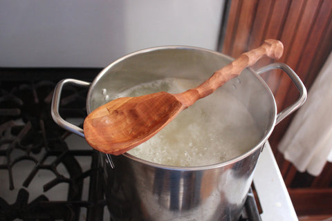 Cooking pot on vintage stove top with deep handmade wooden spoon sitting across it.