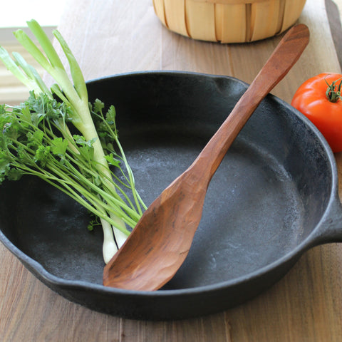 Handmade wooden spoon in a cast iron pan with herbs and onions in the pan