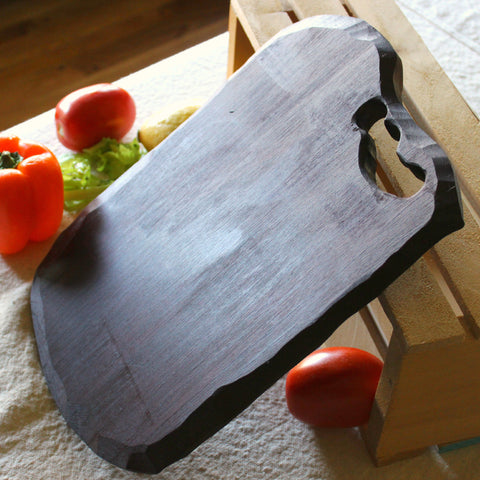 Handmade wooden cutting board leaning against a wooden crate with tomatoes and peppers against a white linen background.