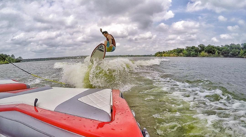 doomswell brand ambassador wakesurfing behind red boat on a neo wakesurf board