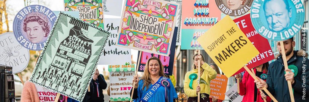 Campaign Shop Independent Image by Holly Tucker and the team at Holly and Co shows a group with colourful placards supporting handmade, vote with your money and independent shops