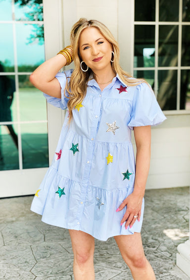 Rewrite The Stars Dress. Light blue, tiered dress with colorful star sequin patches. Features puff sleeves and a collared neck line.