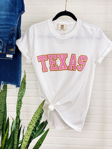 Charlie Southern: Texas Tee, white comfort colored tee, TEXAS written on the front in pink with a burnt orange outline, Charlie southern logo on the back 