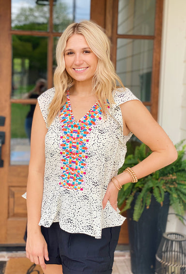 Fiesta Blend Embroidered Top, cream clored top with small black polka dots, ruffle sleeve and ruffle along bottom, colorful geometric embroidered shapes along neckline 