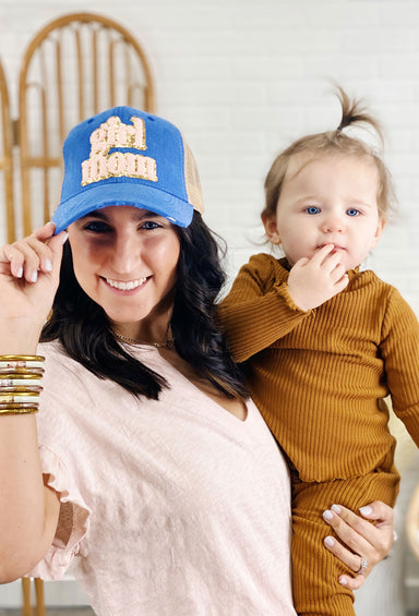 Judth March Girl Mom Hat, Blue and tan trucker hat decorated with "Girl Mom" soft pink patch outlined in gold glitter, and subtle distressing with scratch detail