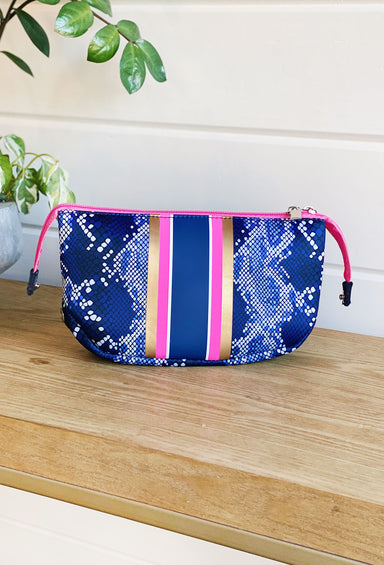 The Sarah Neoprene Small Cosmetic bag features stripes of hot pink, navy, and metallic champagne, on a blue snakeskin background 