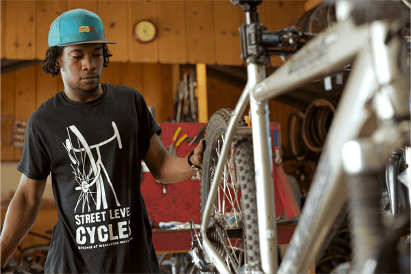 A young Black man fixing up a mountain bike in a bike shop.