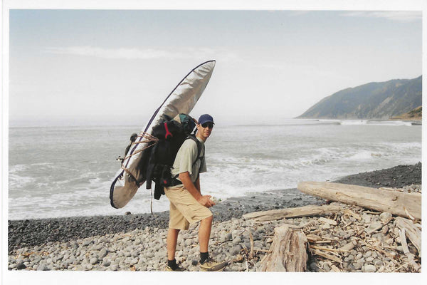 Dave Rumberg with his backpack and surfboard on a beach.