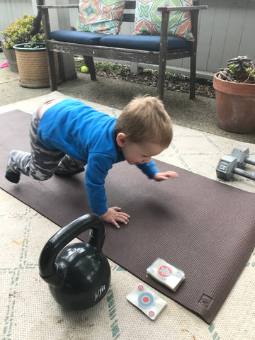 Little boy doing a push up on a yoga mat with a deck of cards next to him.