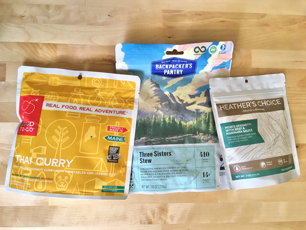 Four packs of different backpacking food packs on a counter