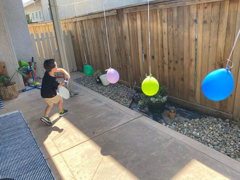 Aiden swinging a racket at different colored, hanging balloons.