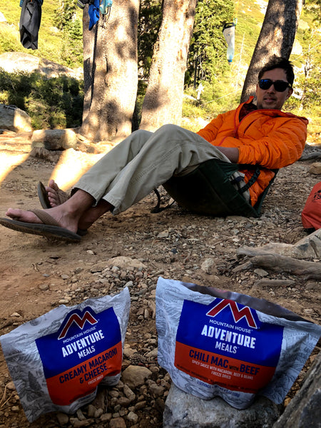 Susan's husband sitting in a camp chair with backpacking food packs