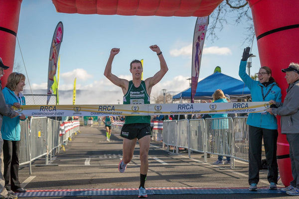 Andrew crossing the finish line banner with his arms up