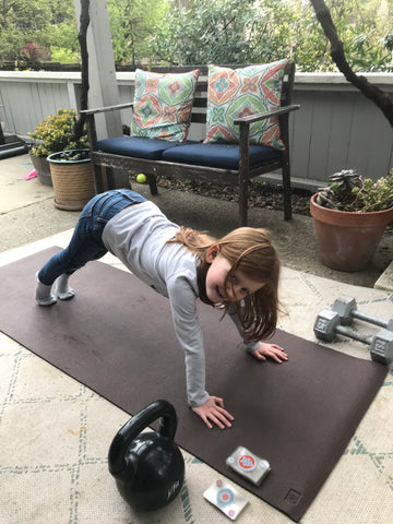 Little girl doing a push up on a yoga mat with a deck of cards next to him.