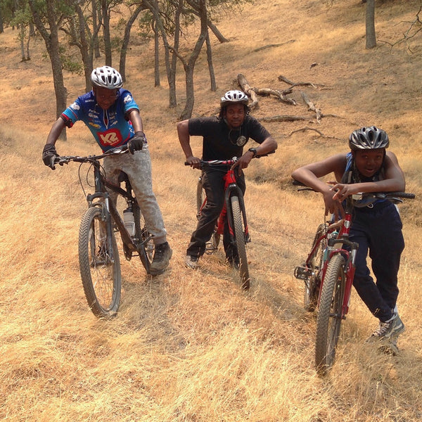 Three young Black boys mountain biking through a trail.