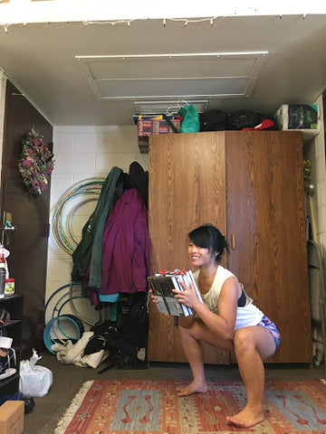 Rachel using a pile of books as a makeshift weight in lieu of a kettle bell in a squat exercise.