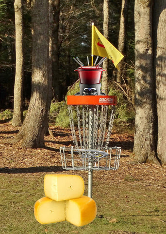 fondue pot on top of disc golf basket with wheel of cheese beside it for april fools day