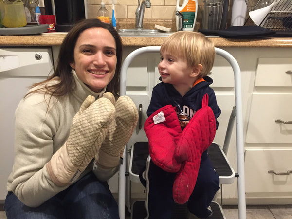 Nicole and Emmett cooking in the kitchen, both wearing oven mitts