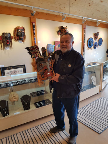 Bill Henderson standing with his Hunter of the Woods mask at the Spirits of the West Coast Art Gallery in Courtenay, BC. 