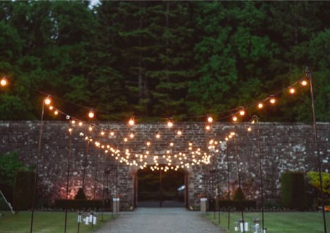 Festoon Lined Walled Garden Walkway with brollybucket hired umbrellas and rustic willow umbrella stands