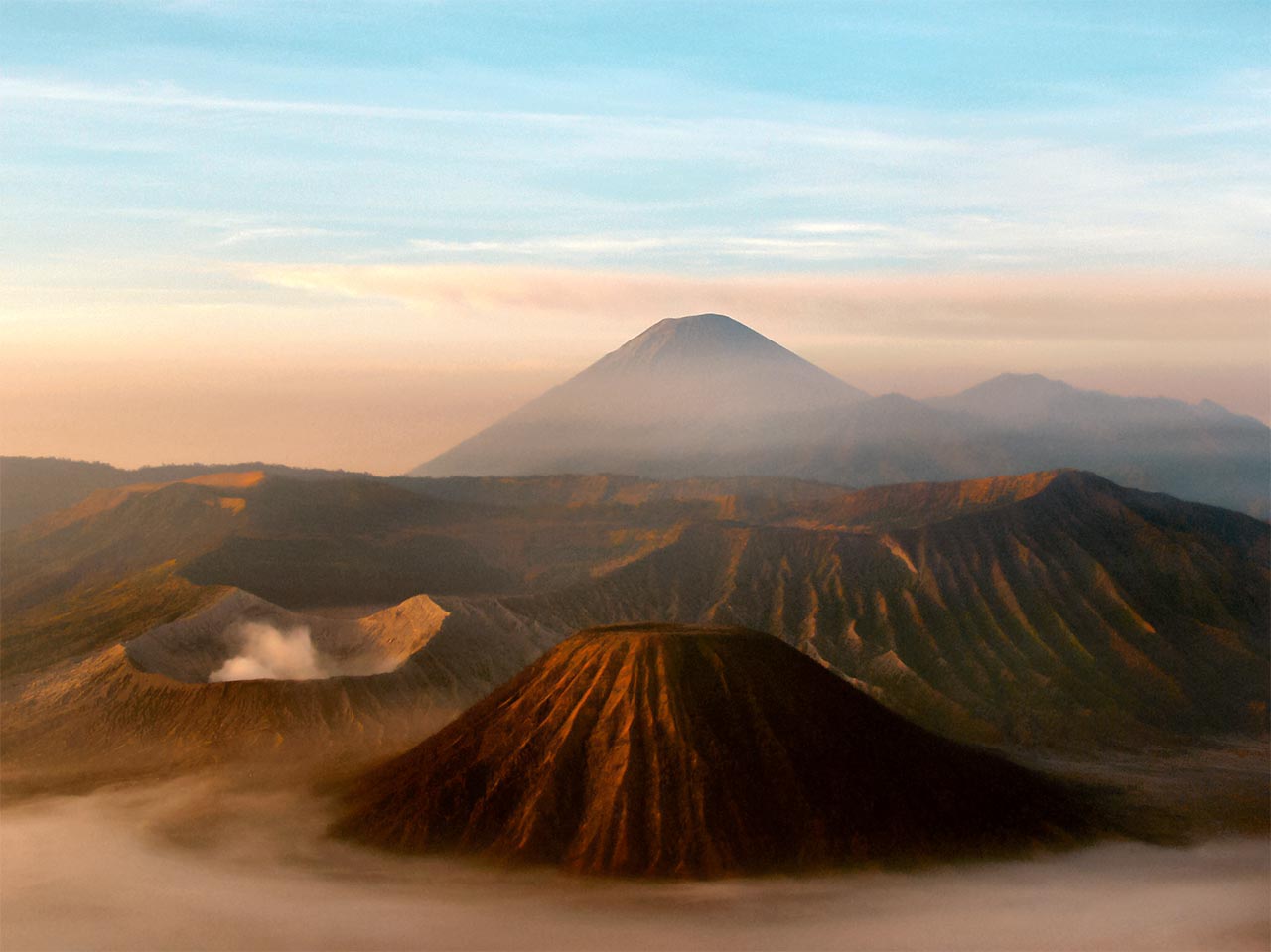 Steam rises from Mount Bromo's crater (in the foreground). It is one the most active volcanoes in the world. Mount Semeru stands tall at the background.