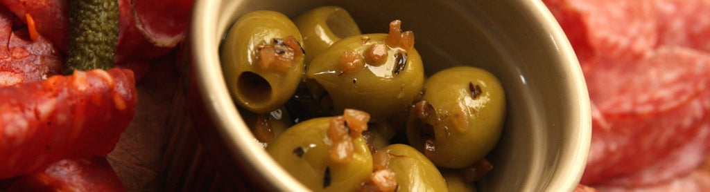 A pot of smoked olives served with sliced smoked meats