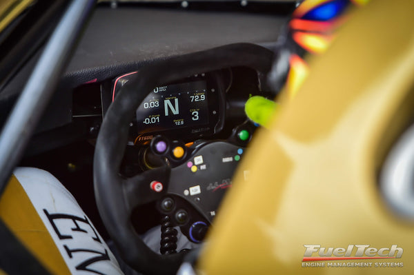 Interior de um carro de corrida marrom. Atrás do volante, o equipamento de injeção eletrônica programável da FuelTech.