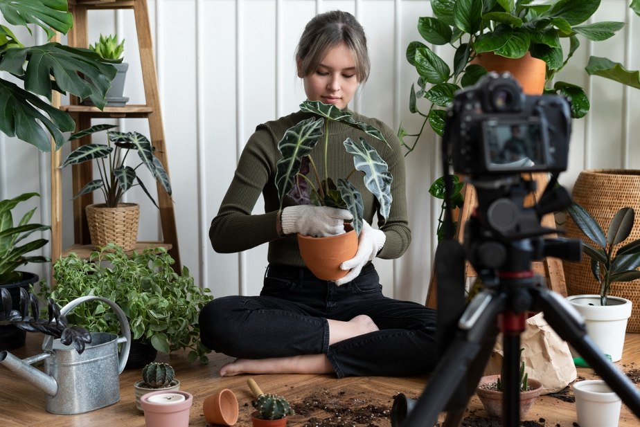 Digital influencer segura um vaso de plantas em frente a uma câmera