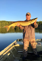 Jim Broberg of Dubro Fishing Products standing in a boat with a big muskie caught on big bucktail made with their bucktail tool