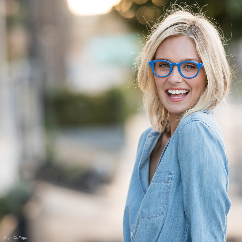 Blonde woman wearing Collage blue light reading glasses by Peepers outside in a denim shirt