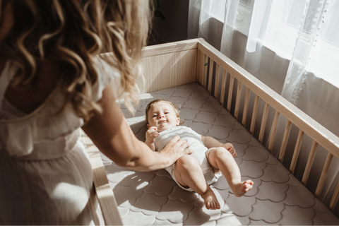 mom laying down baby in nursery