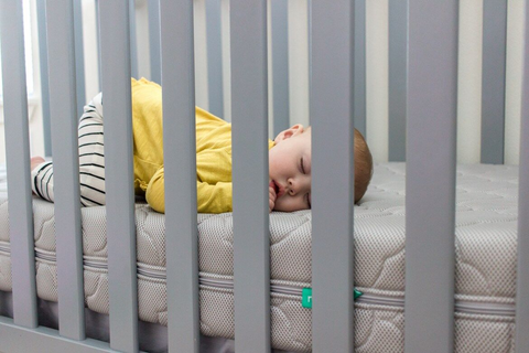 baby sleeping on a newton baby crib mattress in a mini crib