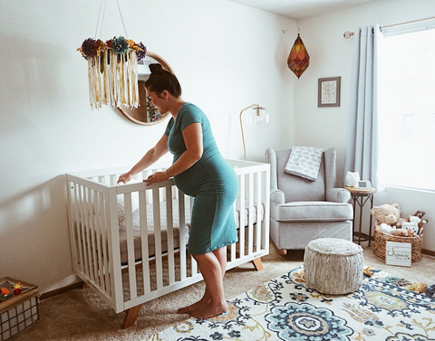 pregnant woman setting up a mini crib in a small nursery