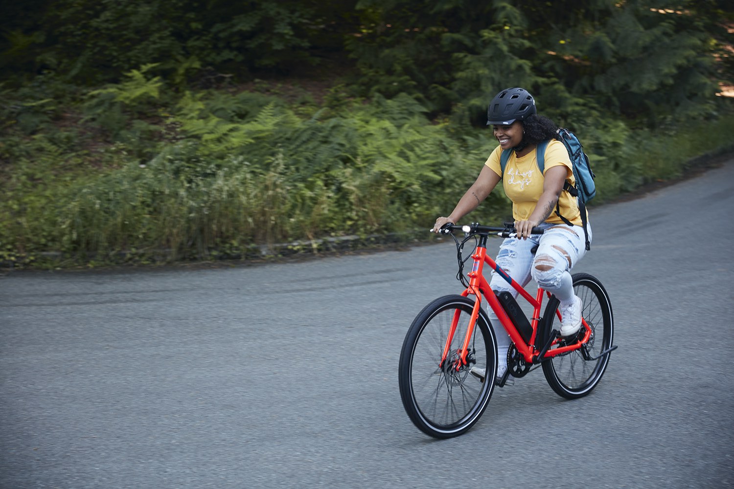 A woman smiles as she rides a red RadMission down a rural street. 