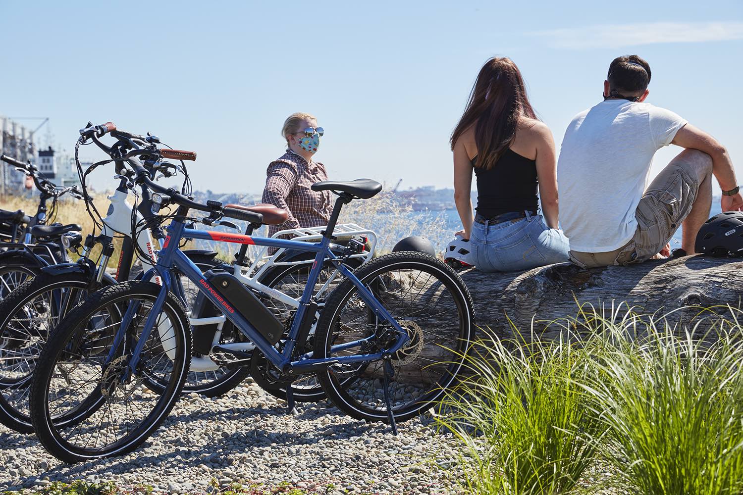 A group of friends meet along the beach, with their ebikes perched to the side.