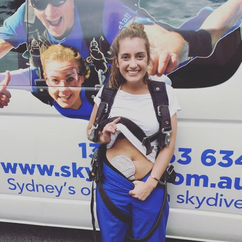Renee showing off her stoma cover while standing in front of a skydiving center