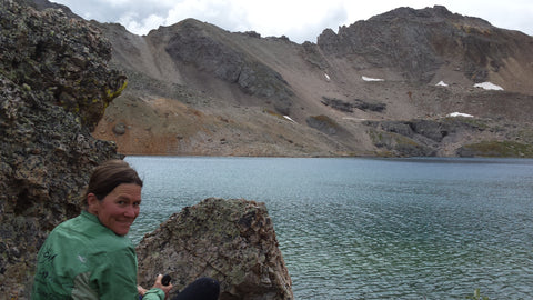 SOM Footwear co-founder Nathalie Bouchard sits by a lake in the colorado backcountry.