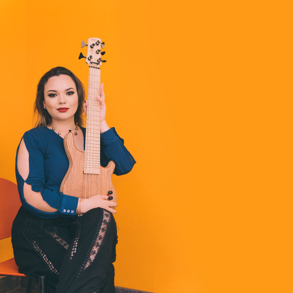 Kala U•Bass Artist Lilo DeLima posing with her Koa 5 Strings U•Bass in front of an orange background.