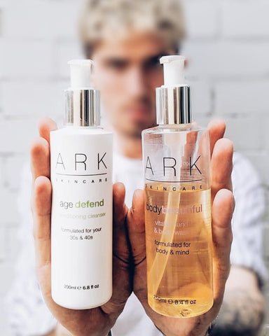 Male model holding ARK Skincare's Age Defend Cleanser and Body wash 